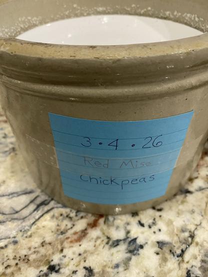We see a blue note taped to a crock. The note reads 3 - 4 - 26 red miso chickpeas.